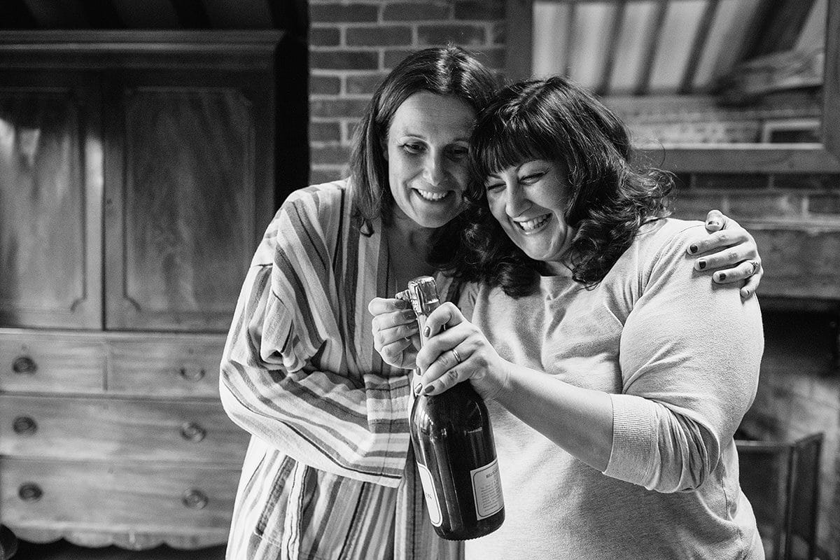 the two bridesmaids open the bottle of champagne