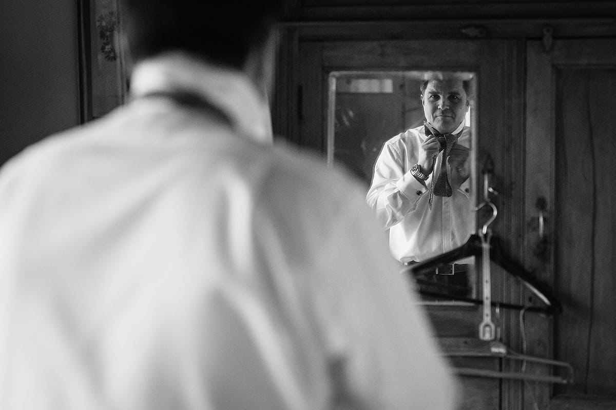 the groom adjusts his tie in the mirror