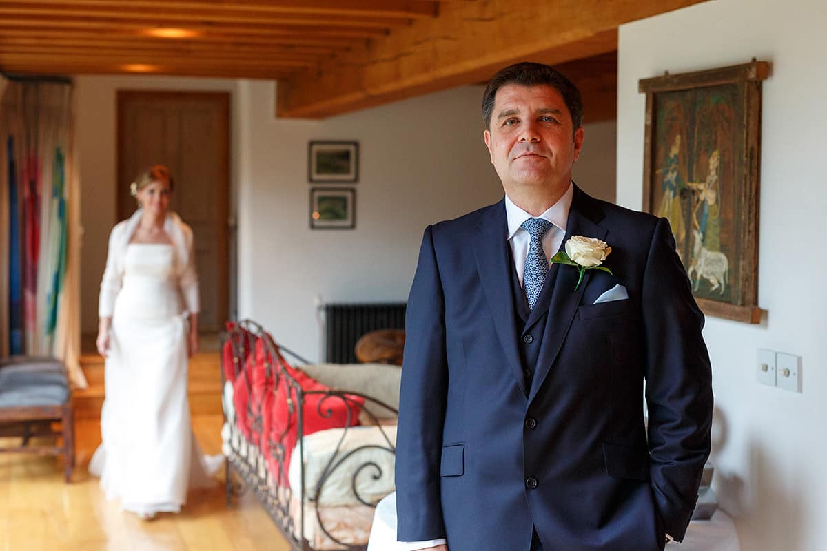 the groom waits with the bride approaching in the background