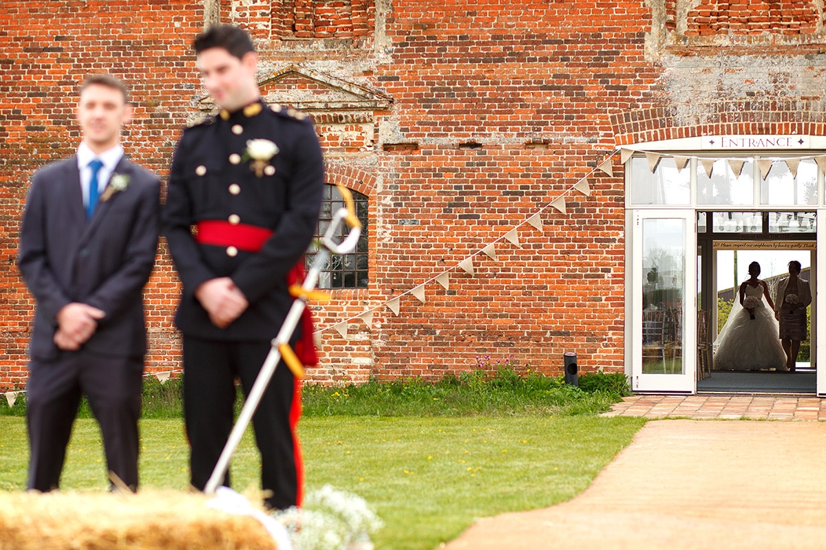 the groom waits with the bride in the background