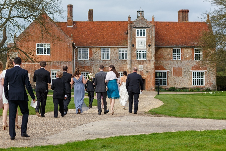 wedding guests walk towards bruisyard hall for the drinks reception