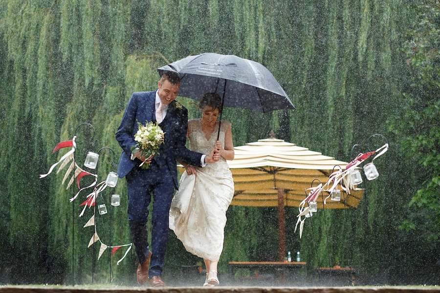 bride and groom running through the rain at their tuddenham mill wedding