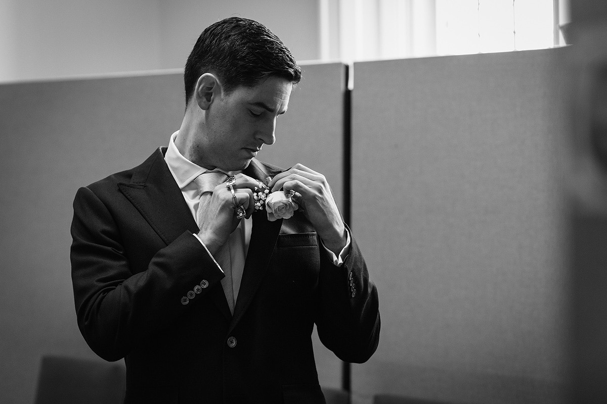 the groom attaches his buttonhole in the norwich registry office waiting room