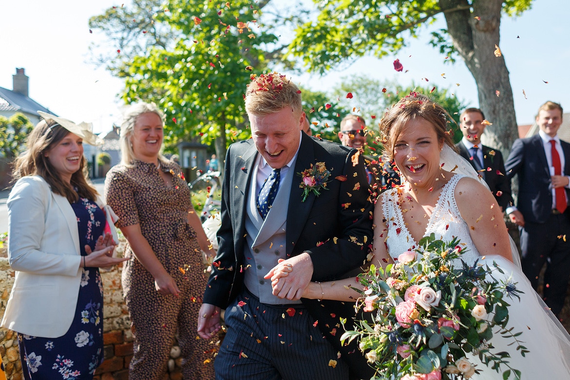 bride and groom run through the confetti outside aldeburgh church