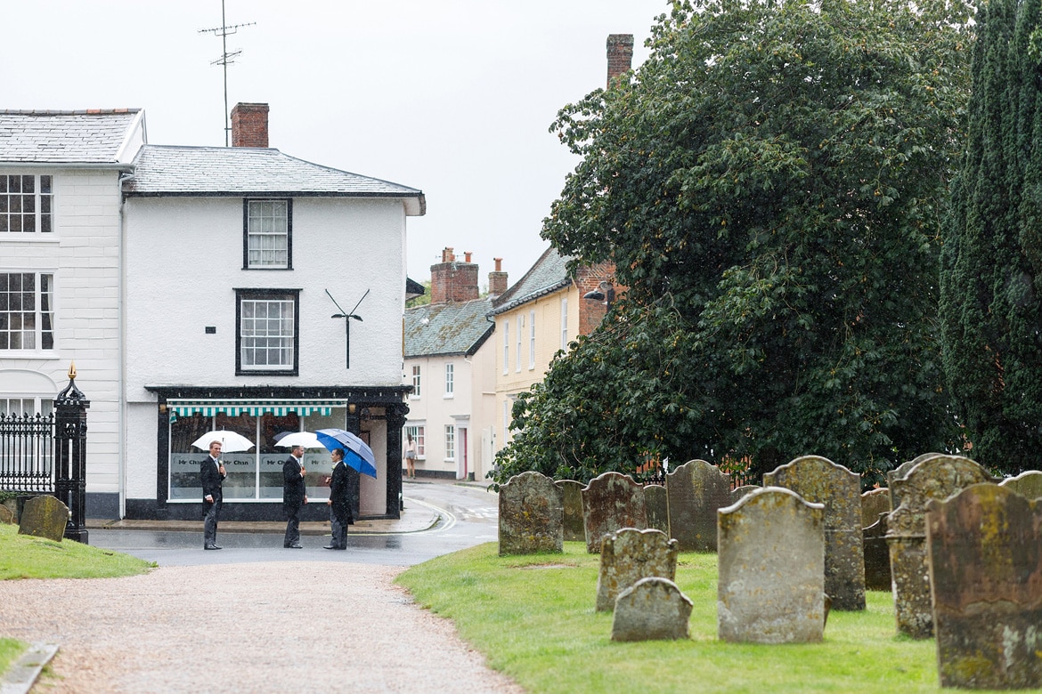 groomsmen wait in the rain outside framlingham church