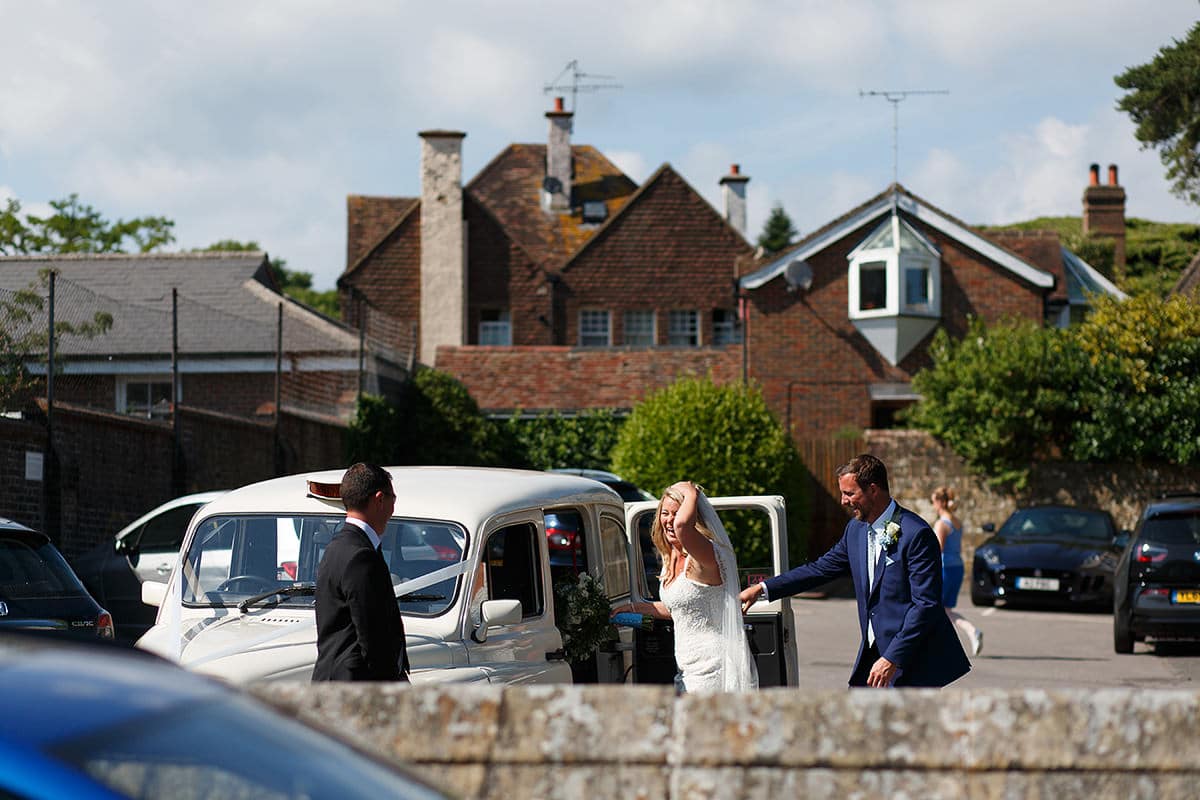 bride and groom get into their white wedding taxi