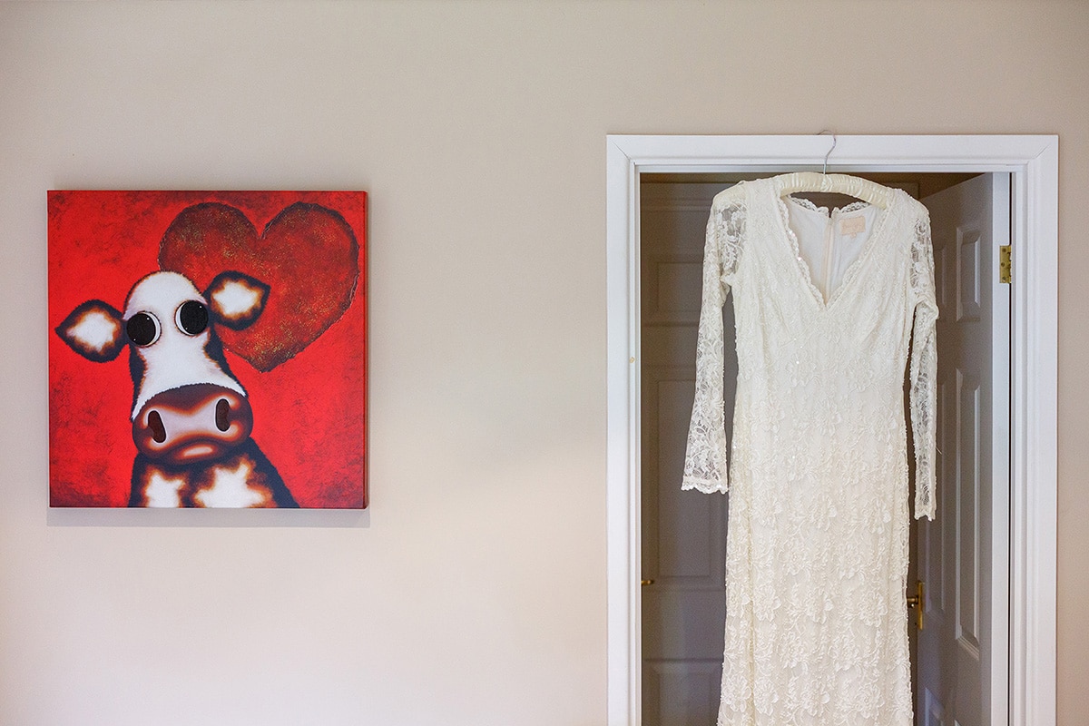 Wedding dress hanging in a door frame with a cow photo next to it