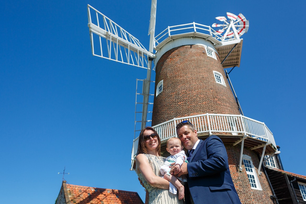 bride and groom with their baby in front of cley windmill