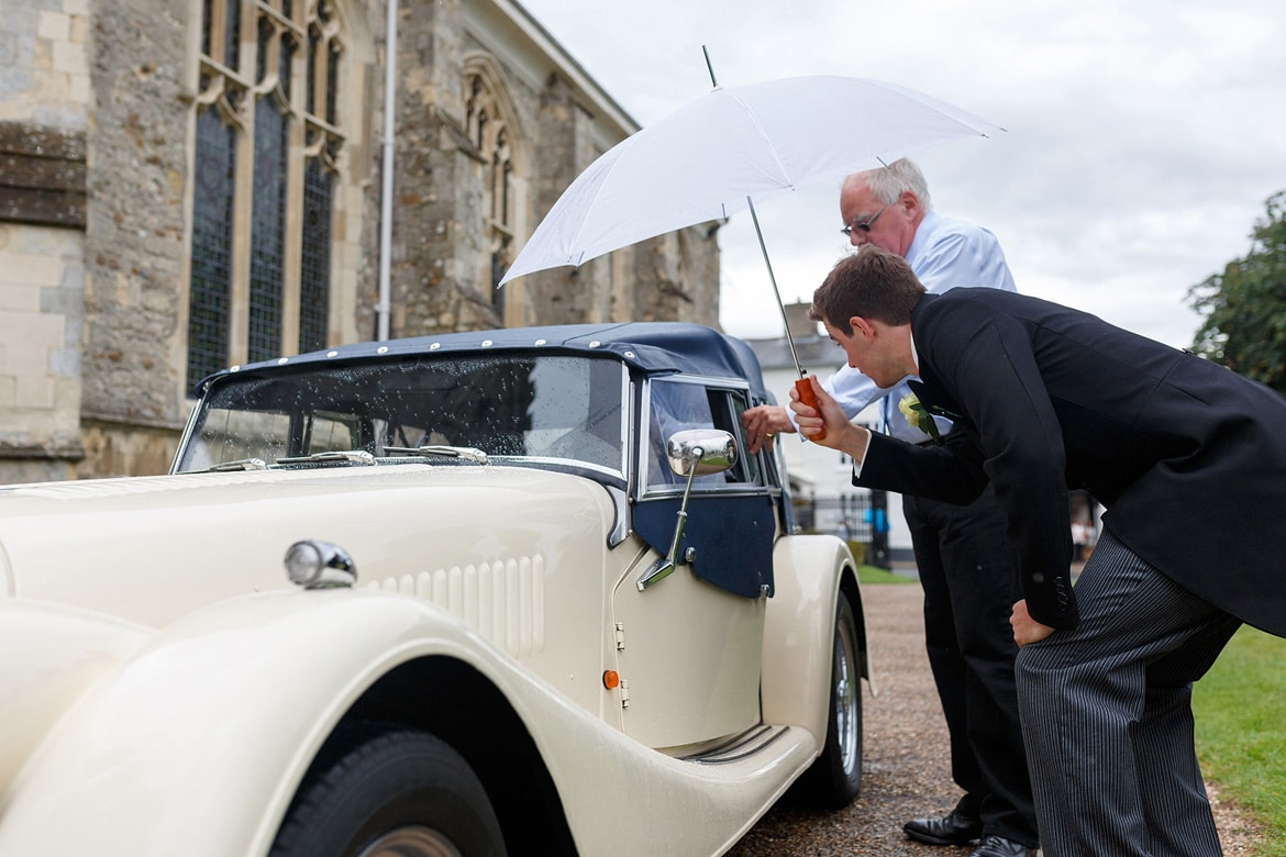 a groomsman offers his umbrella to the bride