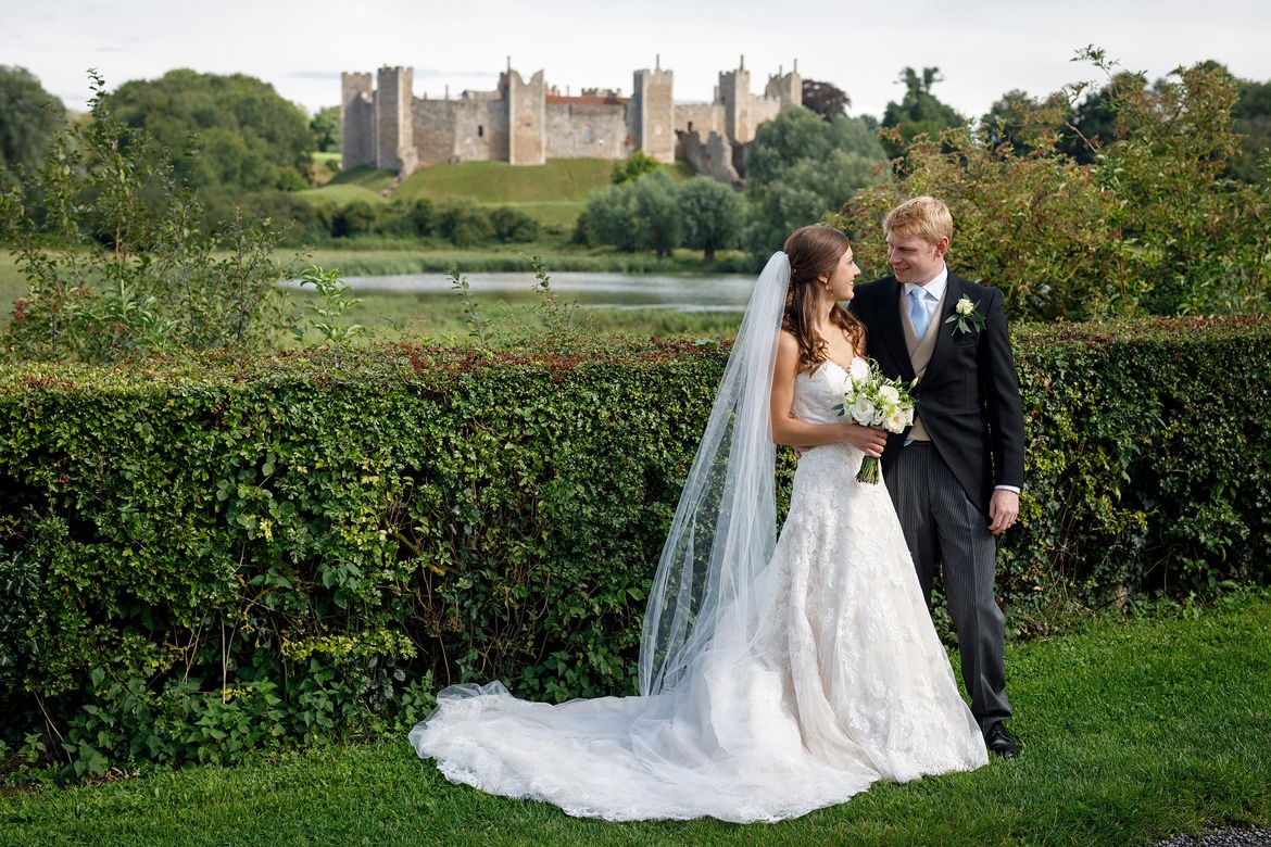 bride and groom pose with framlingham castle in the background