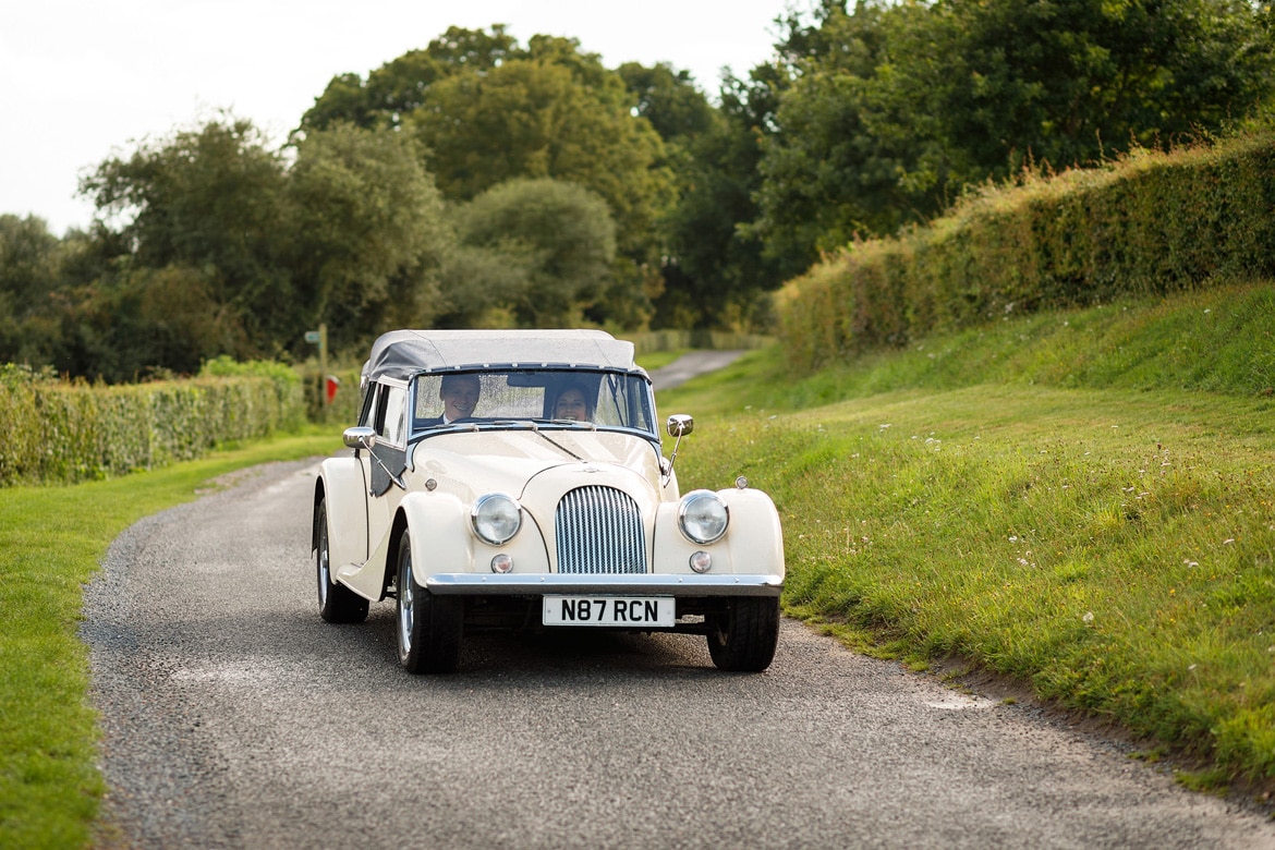 a vintage morgan drives along a lane behind framlingham castle