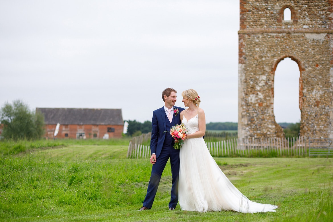 bride and groom in front of godwick barn and the ruins