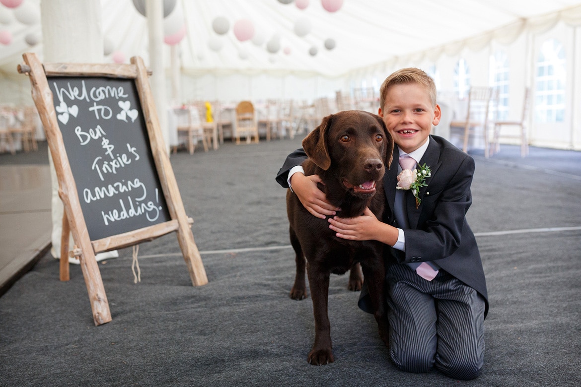 a pageboy hugs the family dog in the marquee