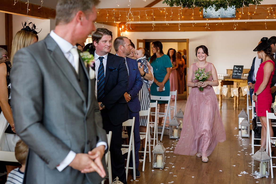 the bridemaid smiles at the groom as she walks down the aisle