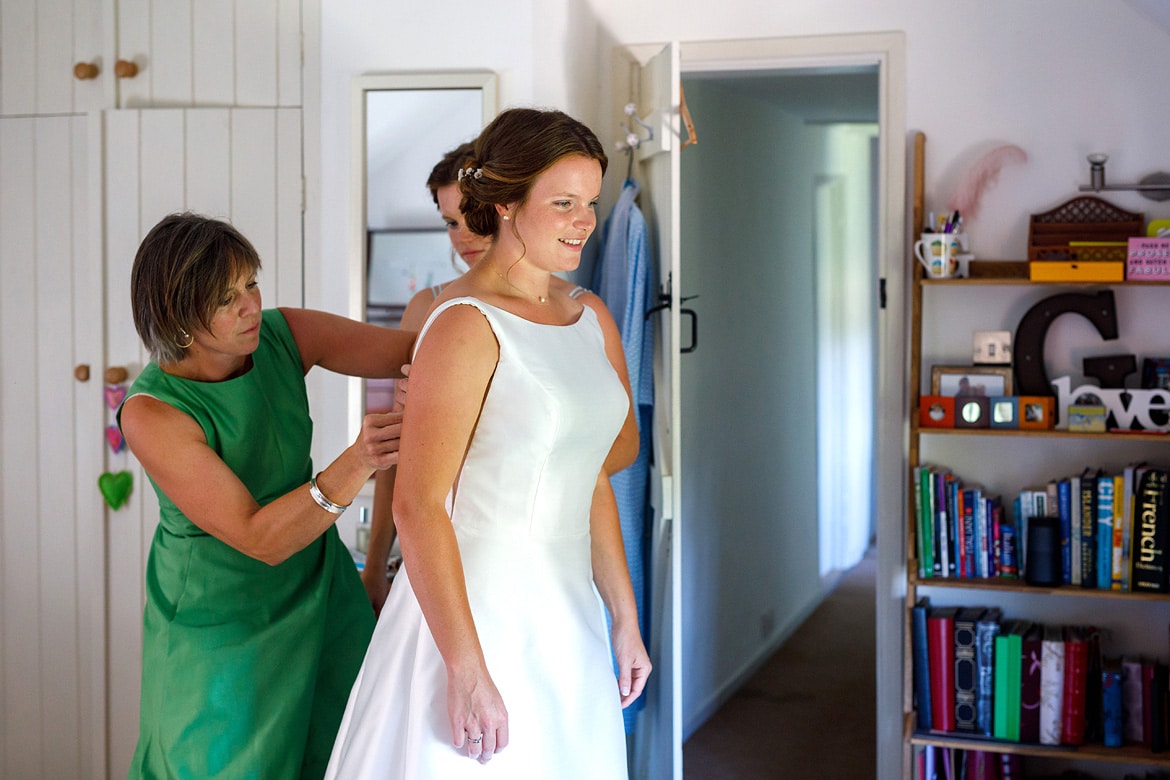 the brides mother and sister help her with her wedding dress