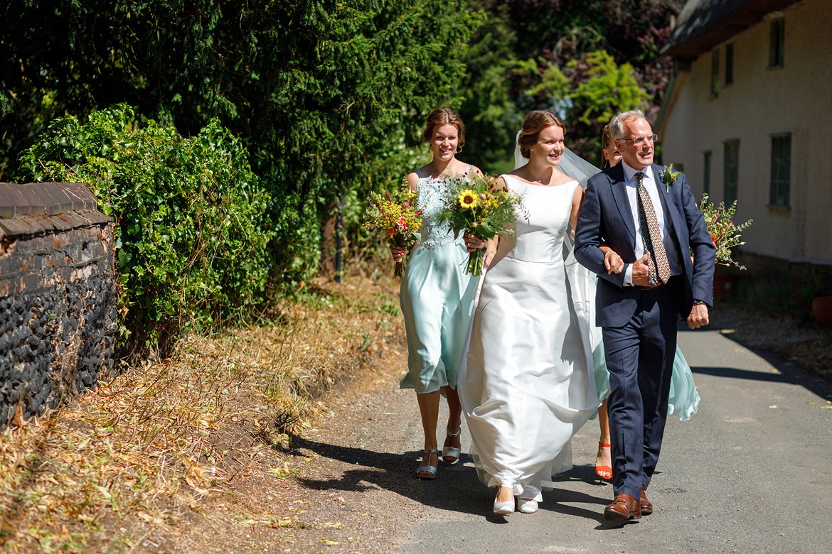 the bride and her father walk to old buckenham church