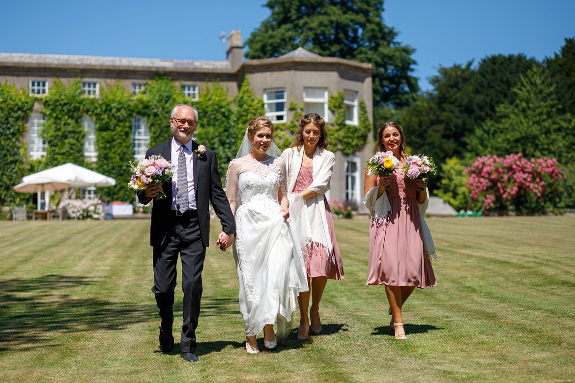 the bride walks down pennard house lawn with her father and bridesmaids