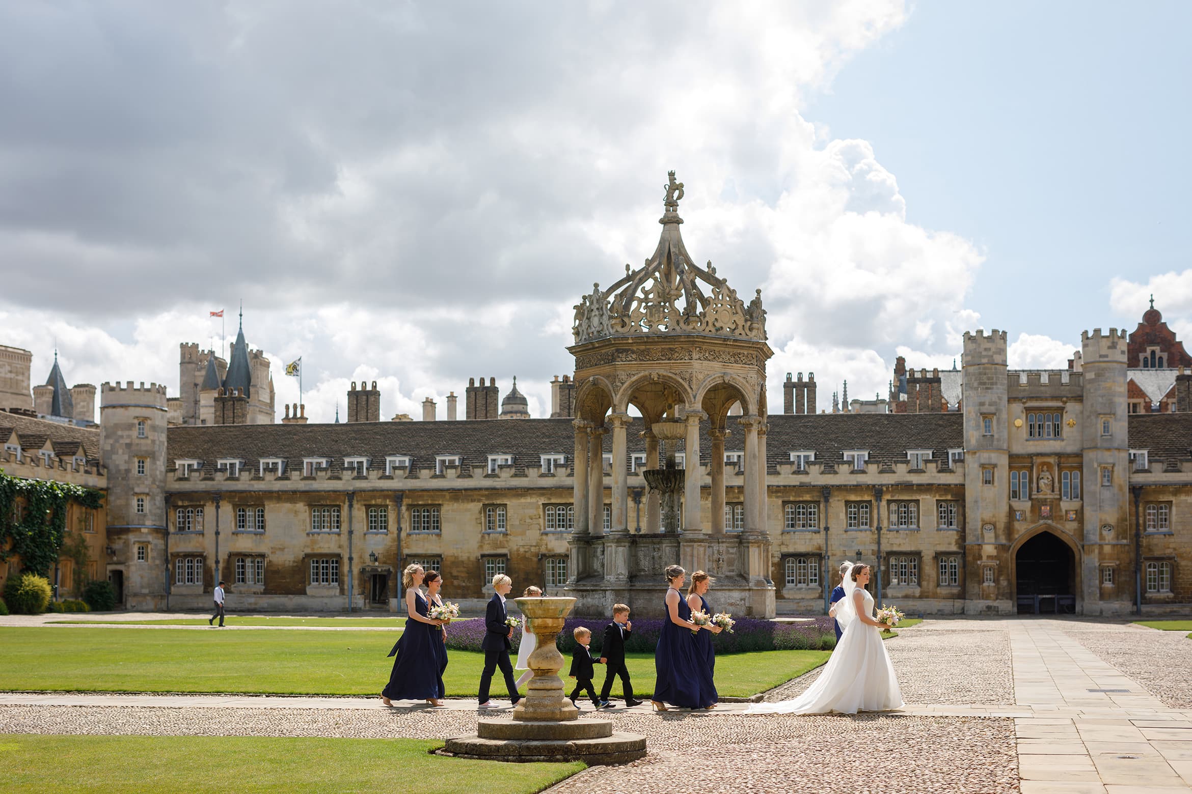 the bride walks in front of the fountain at trinity college cambridge
