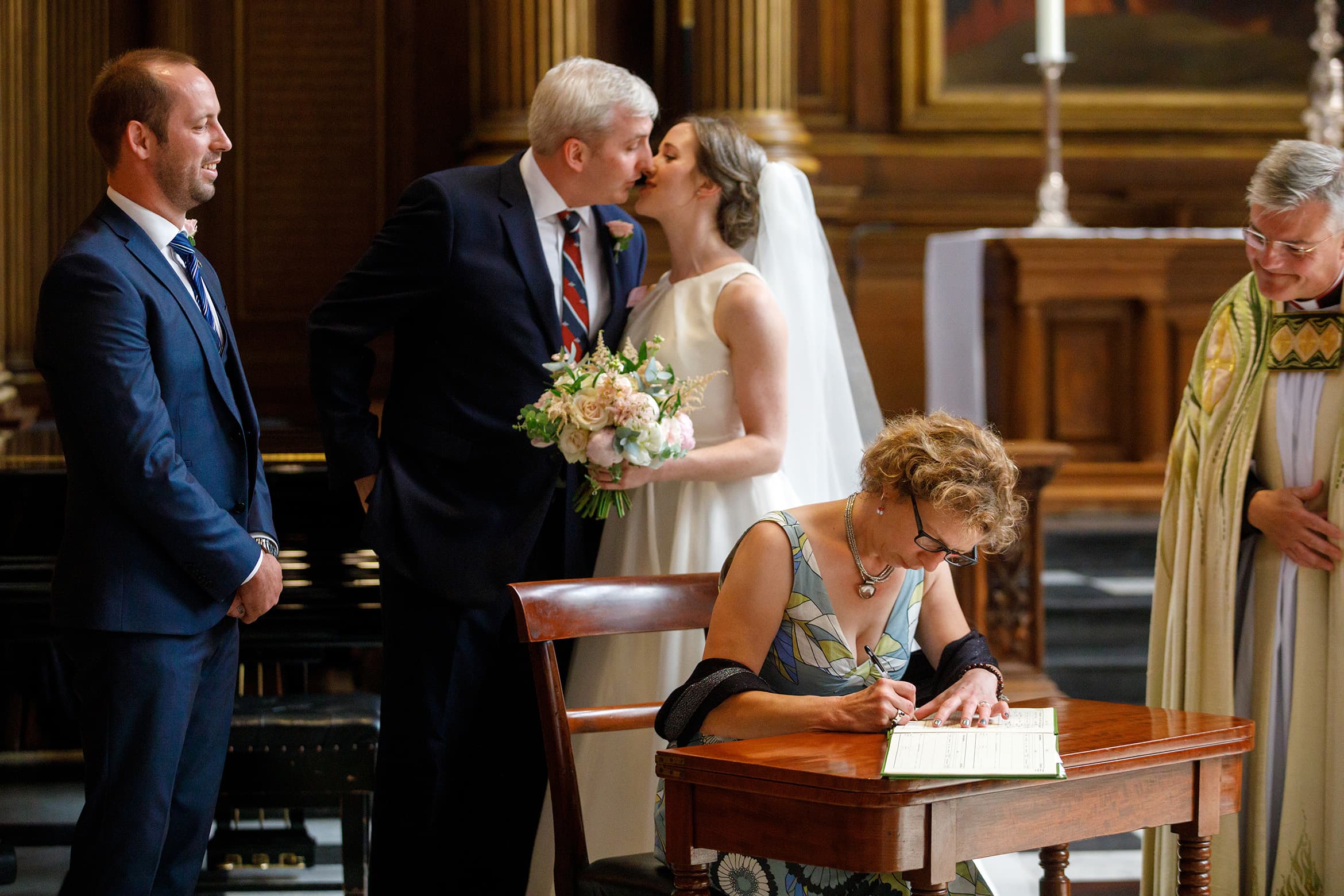 bride and groom kiss as a witness signs