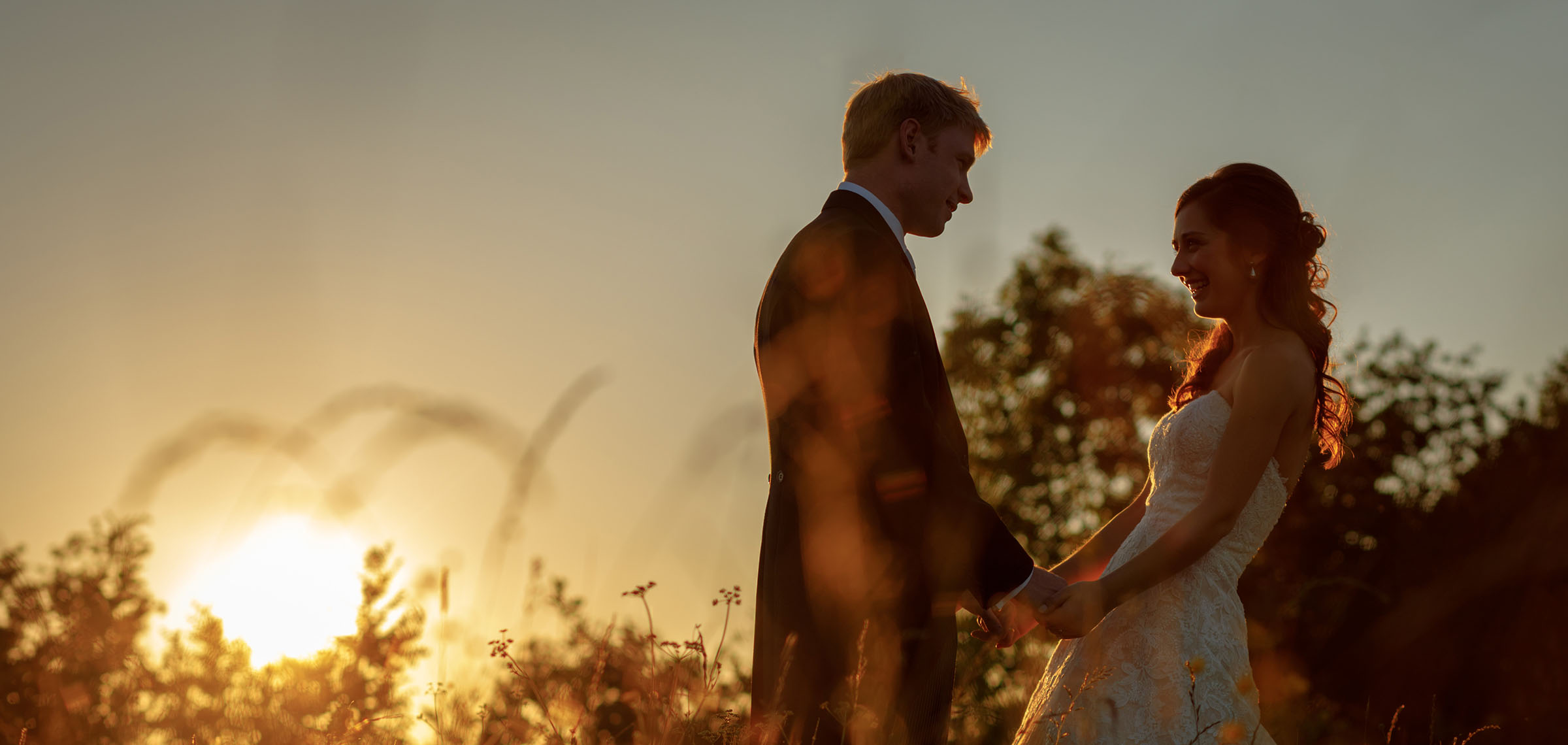 bride and groom in a field at sunset